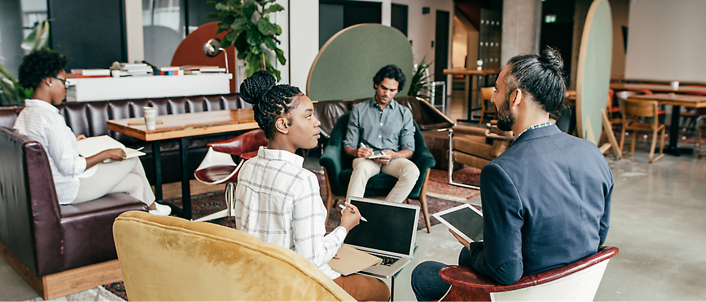 Un groupe hétérogène de quatre professionnels engagés dans une discussion dans un espace de bureau moderne.