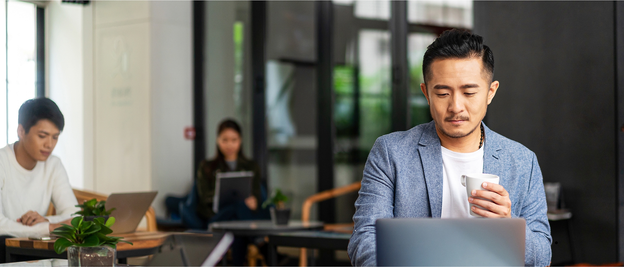 A man in a suit looking at a laptop while holding a cup.