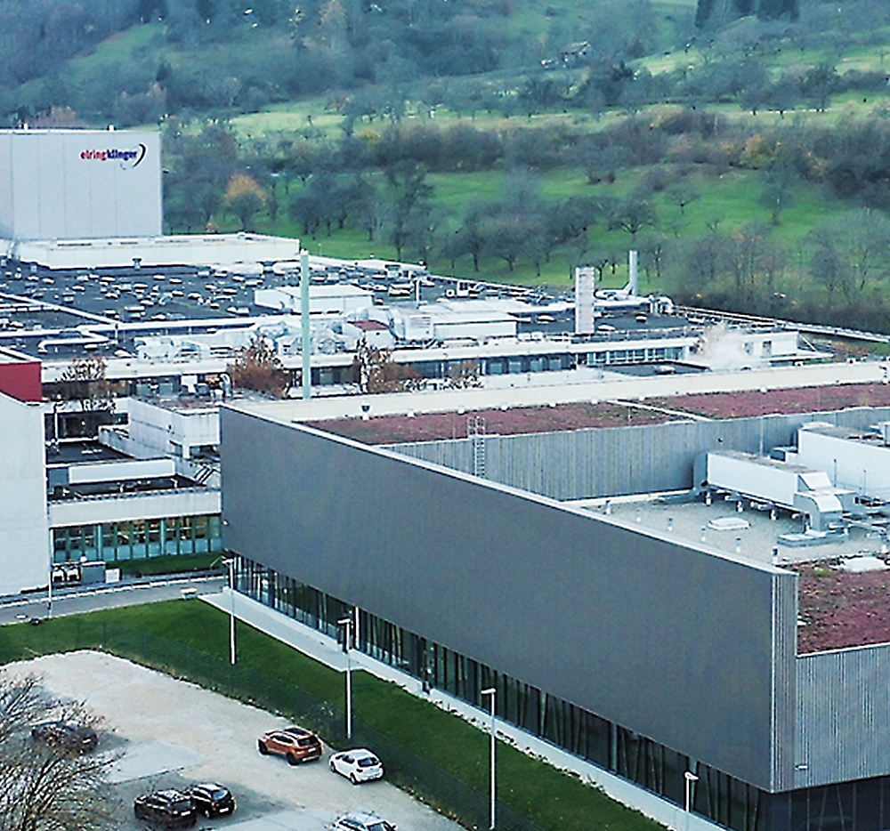 A quaint suburban house with a well-manicured garden, featuring two chairs on the lawn and vibrant flowering 