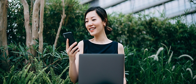 一位女士拿着手机看着笔记本电脑。