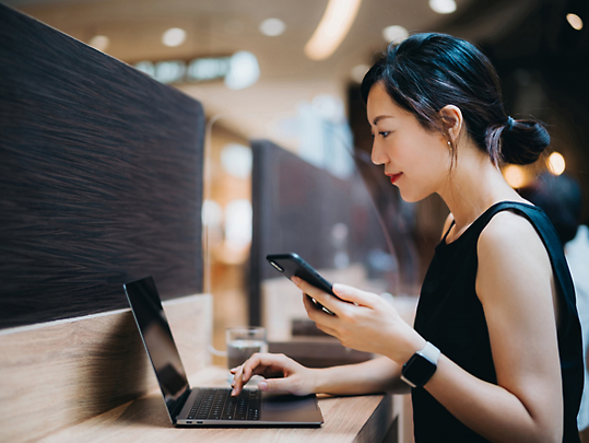 Une personne assise à une table alors qu’un ordinateur portable est ouvert sur la table et qu’un téléphone se trouve à portée de main