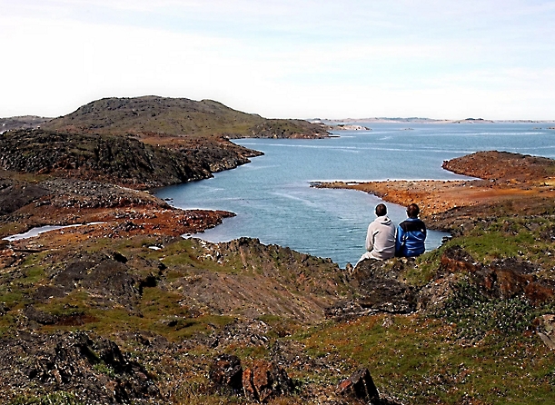 A couple of people sitting on a cliff overlooking a body of water.