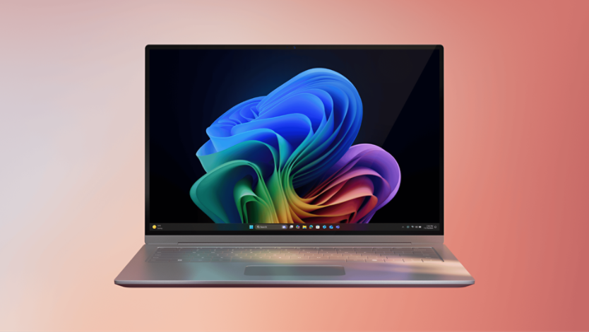 A Copilot+ PC device open with the Microsoft rainbow bloom. The screen shows the Windows 11 taskbar, and the background is a gradient from light pink to peach.