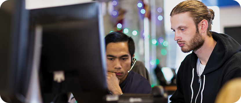 Two men focused on a computer screen in a modern office setting, one asian and one caucasian