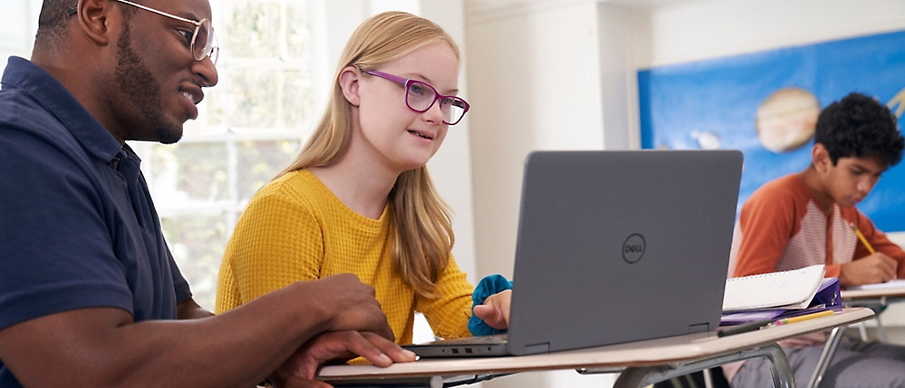 A girl in a yellow shirt and glasses looking at a laptop.