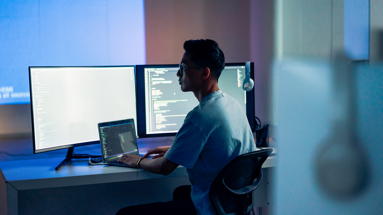 Person sitting at a desk working on a laptop with multiple computer monitors displaying code.