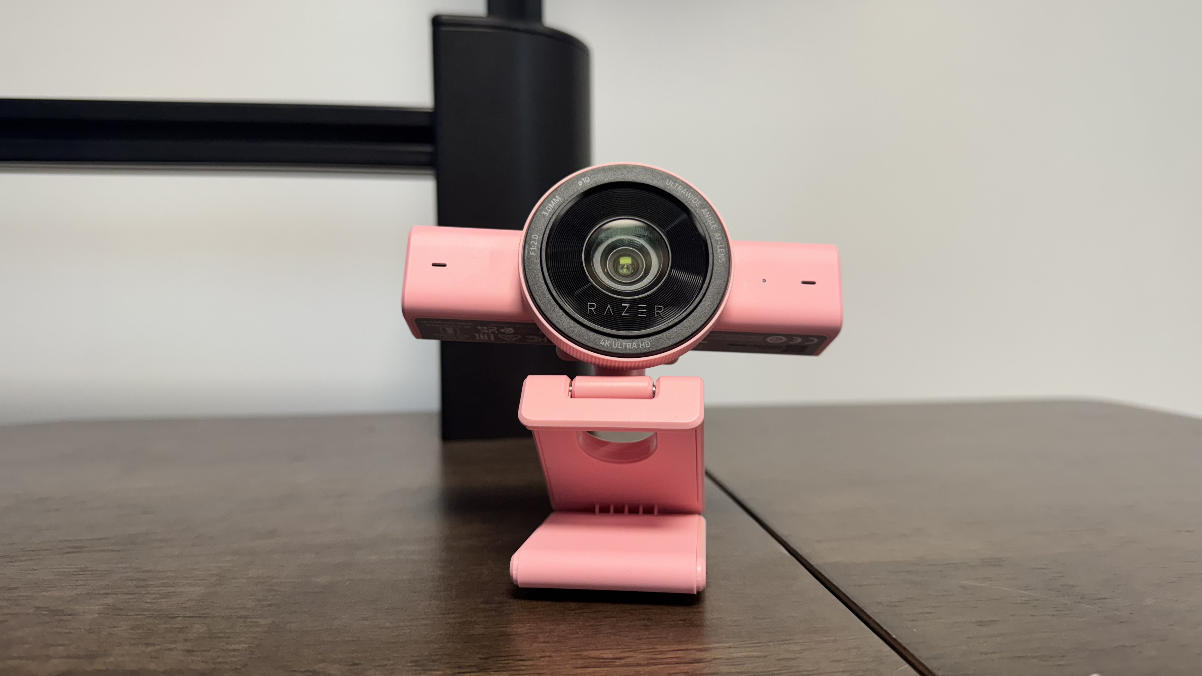 The pink Razer Kiyo V2 on a wooden desk, with the lens pointing to the centre and up