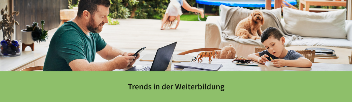 Ein Mann arbeitet am Esstisch und informiert sich über berufliche Weiterbildungen, während im Hintergrund Kinder und ein Hund zu sehen sind.