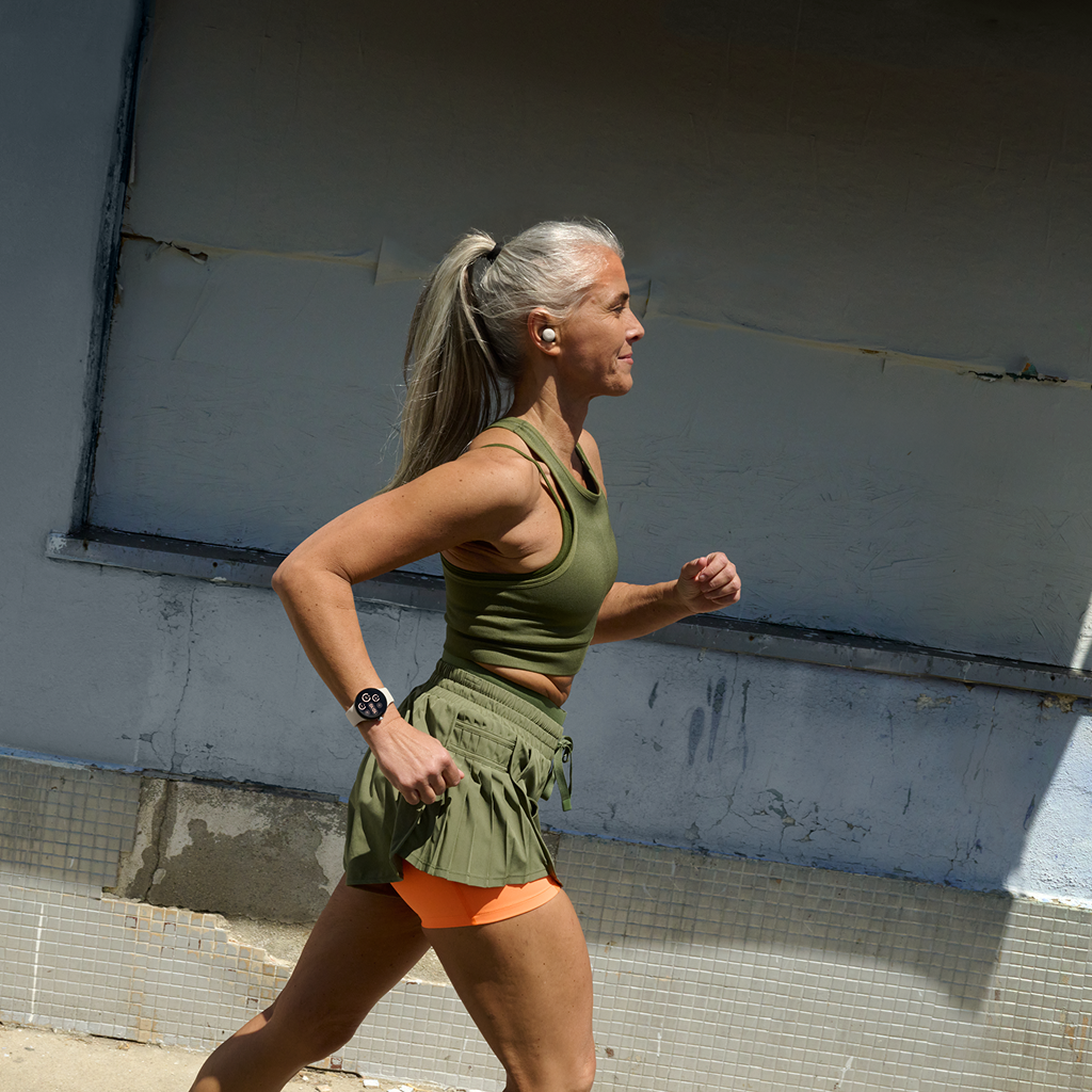 A woman in green athletic gear jogs past a wall while wearing a smartwatch.