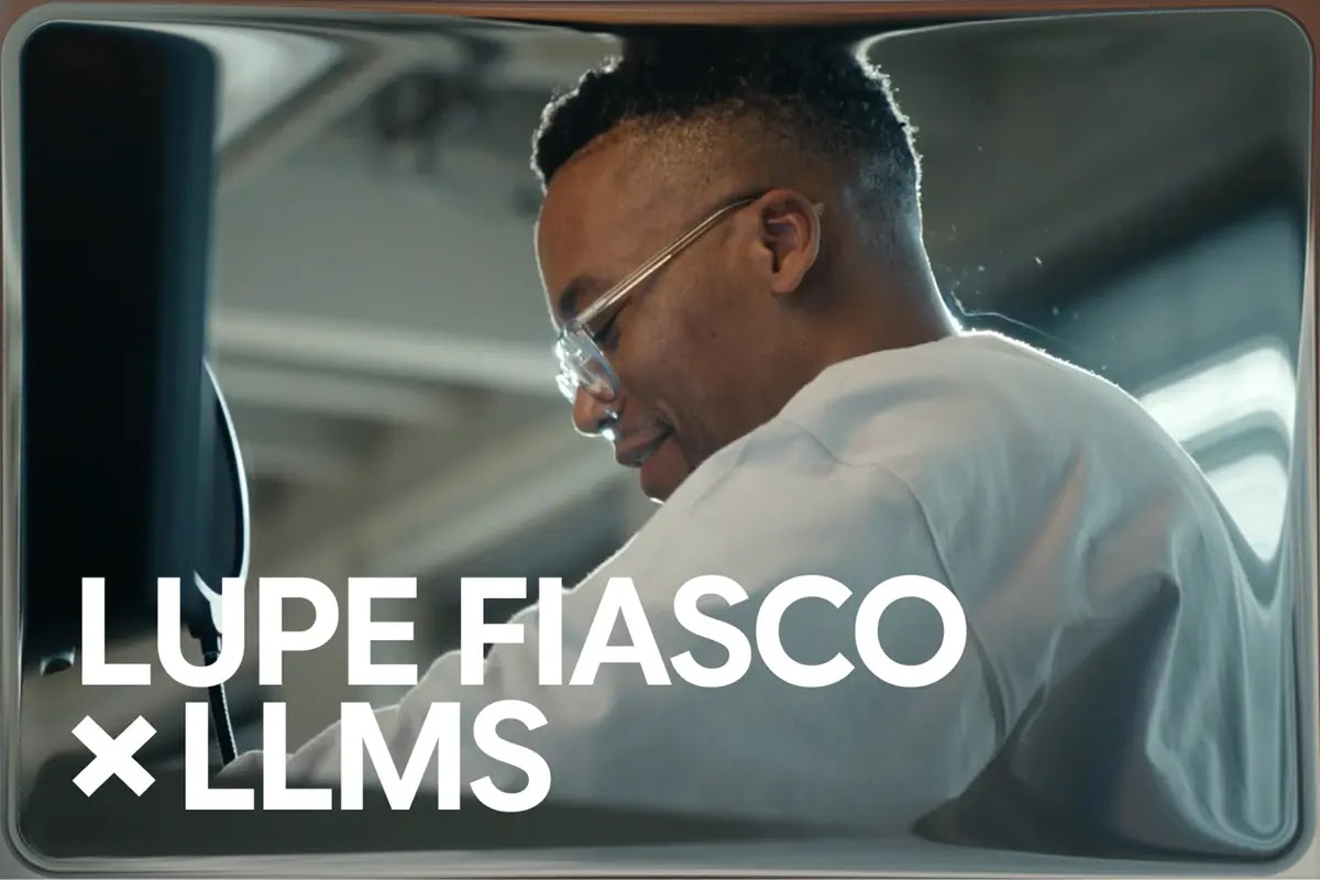 A side-profile view of rapper Lupe Fiasco wearing clear glasses and a white sweatshirt, smiling faintly in a bright studio environment. Bold text overlays the bottom left: "LUPE FIASCO × LLMS".