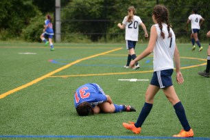 A female soccer player in a blue and red jersey lies on the grass field, clutching her leg in pain.