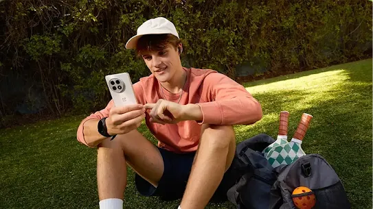 A young man using an Android phone on a grassy field.